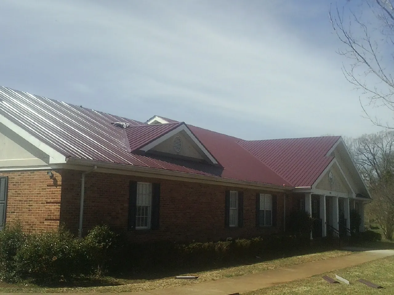 Red metal roof with gabled entries on a long brick building, from a Hail Damage Roof Repair job in Beaverdam