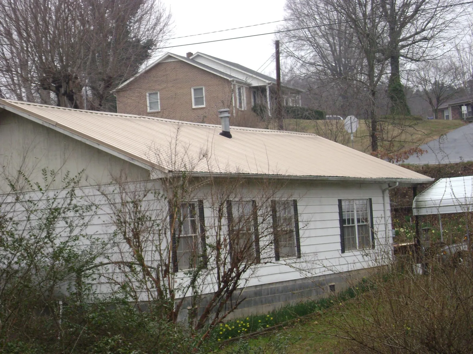 Tan metal roof on a white sided house set into a hillside — Commercial Roofing by Roofing Brothers in Beaverdam