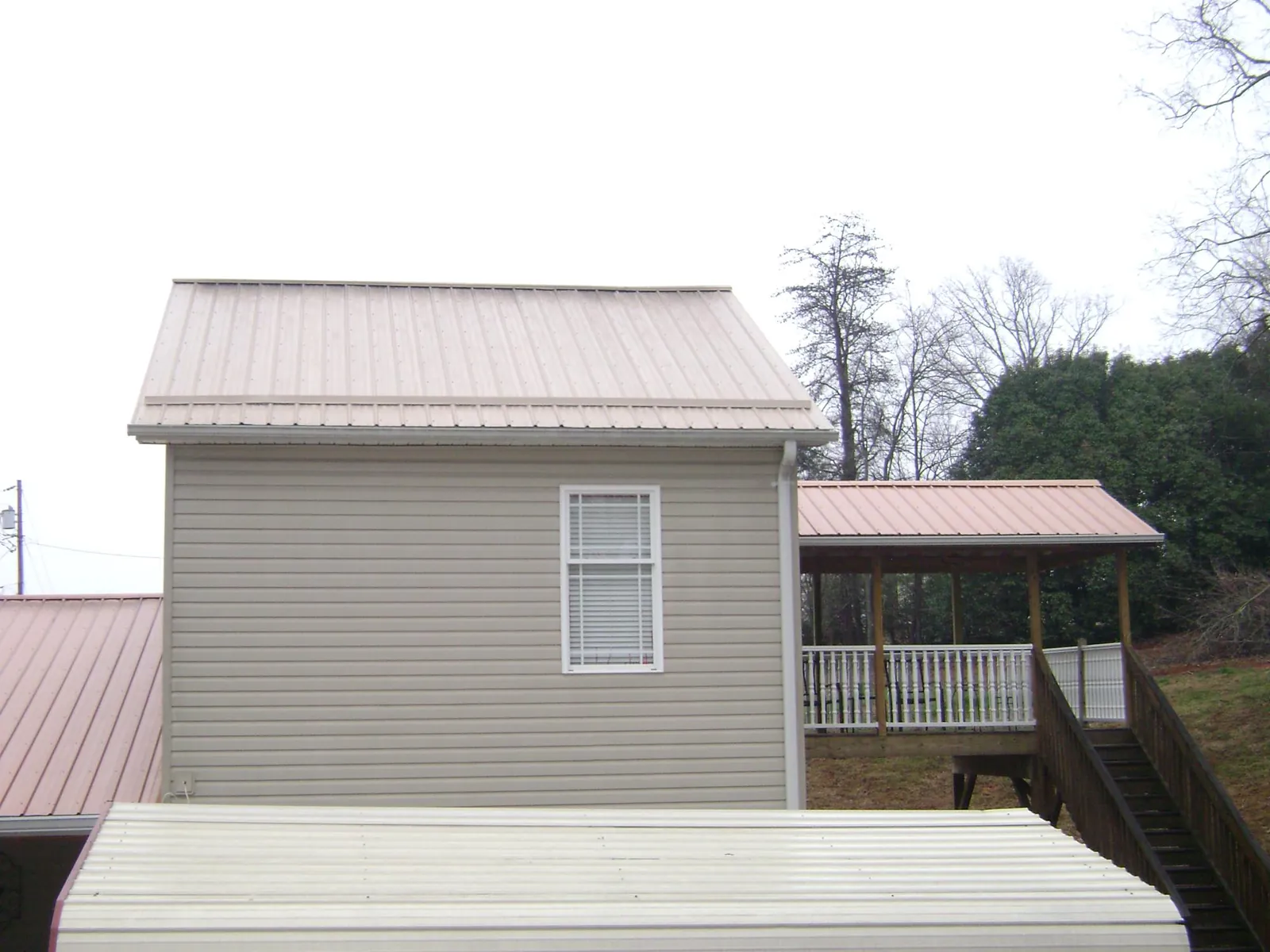 Tan metal roofs on a two story addition and attached porch, from a Roof Replacement job in Beaverdam